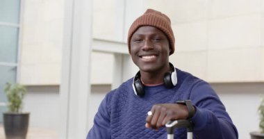 Kayıt başlıyor. Afro-Amerikalı erkek, elinde bavulla kapıda oturuyor ve gülümsüyor. Seyahat, macera, keşif, eğlence, şehir, modern, gündelik