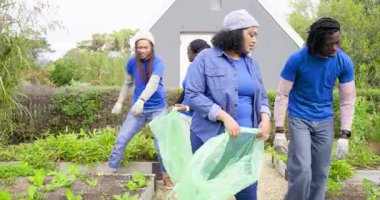 Gönüllü bahçıvanlar barakada toplanıyor. Temizlik için eldiven takmış yabani otları çantaya dolduruyorlar. Topluluk, takım çalışması, sürdürülebilirlik, açık hava, manzara, koruma, uyum