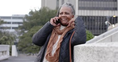 Kıdemli Afrikalı Amerikalı kadın telefona cevap veriyor ve terasta haberlere gülüyor. Portre, profesyonellik, kentsel, samimi, neşeli, zarafet, yaşam tarzı