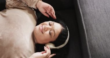 Kulaklıklardan müzik dinlemek, gri koltukta oturan orta yaşlı bir kadının gülme krizine girmesi. Rahatlık, rahatlık, rahatlık, işitsel, sağIık, modern, yaşam tarzı