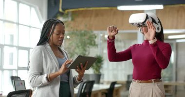 Çeşitli bayan meslektaşlar, açık planlı ofisteki tabletlere dokunarak VR kulaklıklarına tepki veriyorlar. Gelecek, işbirliği, yenilik, teknoloji, çalışma alanı, etkileşim, profesyonel
