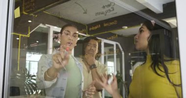 Beyin fırtınasını takiben, çeşitli iş arkadaşları işaretler kullanarak cam beyaz tahta üzerinde 12 aylık bir plan hazırlıyorlar. İşbirliği, beyin fırtınası, takım çalışması, şirket, iş, planlama, modern