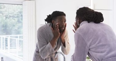 Cilt muayenesi için lavaboya krem sürerken aynayı kontrol eden Afro-Amerikalı bir adam. Cilt bakımı, güzellik, yansıma, refah, minimalizm, kişisel bakım.