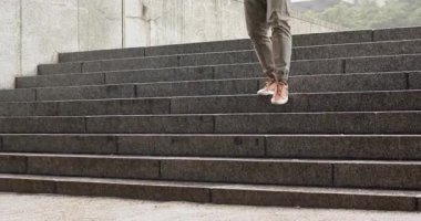 Afro-Amerikalı bir adam şehir meydanında taş basamaklardan iniyor, ayak basıyor, ilerlemeye hazırlanıyor. Merdiven, hareket, şehir, ayakkabı, mimari, boş zaman, etkinlik