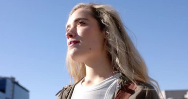 Çatıda yeşil ceketli bir kadın güneş ışığı alıyor ve başını kameraya çevirip gülümsüyor. Moda, portre, şehir, açık hava, sokak giyimi, zarafet, özgüven