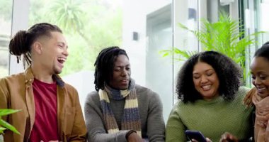 Çeşitli arkadaşlar akıllı telefonlar yetiştiriyor, şakalar yapıyor, telefonları uzatıyor ve cam kapılarla kanepede gülüyorlar. Yoldaşlık, bağlantı, neşe, eğlence, modern yaşam tarzı, pozitiflik.