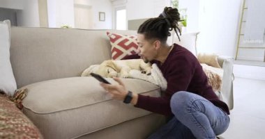 Evdeki kanepede diz çöküp akıllı telefon ekranını dinleyen köpek yavrusunu battaniyeye sarıp fotokopi çeken bir adam. Sevimli, arkadaş canlısı, dijital, rahat, yaşam tarzı, rahatlama, rahatlama