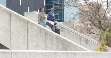 İş arkadaşları bavullarıyla merdivenlerden inerken yaşlı adam genç dinleyicilere rehberlik ediyor. Kentsel, profesyonel, hareketli, takım çalışması, iletişim, danışmanlık, minimalist