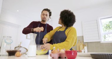 Afro-Amerikalı çift mutfakta tablete danışmanlık yaparken spatula alıp hamuru karıştırıyorlar. Yemek pişirme, takım çalışması, yerli, aşçı, modern, işbirliği, aile