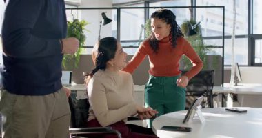 Tekerlekli sandalyeye yaslanıp kahkahalarla tableti tartışan çeşitli iş arkadaşlarını çağıran telefon sinyalleri. İşbirliği, çeşitlilik, takım çalışması, modern, canlı, işyeri, iletişim