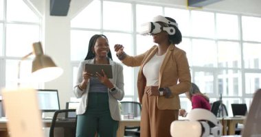 Afro-Amerikalı iş arkadaşları ofiste sanal gerçeklik arayüzü kullanırken kulaklık takıp tableti tıklatıyorlar. Teknoloji, yenilik, işbirliği, dijital, modern, üretkenlik, çalışma alanı