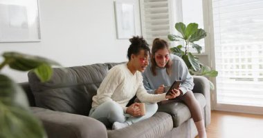 Göz altı yamaları yerleştirdikten sonra, çeşitli bayan arkadaşlar tablet uygulamasına bakıyorlar, kanepede fincanları yudumluyorlar. Arkadaşlar, rahat, rahat, yaşam tarzı, modern, rahatlama, iletişim