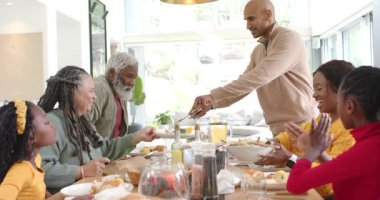 Evde babasıyla yemek yiyen, salata servis eden, ekmek dilimleyen, el çırpan çocuklar. Aile, toplantı, aşçılık, ev, kutlama, sıcaklık, gelenek