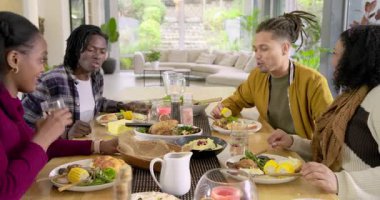 Çeşitli arkadaşlar sohbet ederek kahkaha atıyor, bardakları tokuşturuyor ve evde yemek yiyorlar. Arkadaşlar, kutlama, şenlik, sosyalleşme, yaşam tarzı, modern, canlı