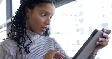 Afro-Amerikalı kadın tableti tıklatıyor, pencereye doğru kayıyor beklenmedik haberlere tepki veriyor ve gülümsüyor. Gelecek, teknoloji, yenilik, profesyonellik, çok yönlülük, zarafet, bağlantı