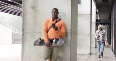 Afrikalı Amerikalı erkekler kolona yaslanıyor ve telefonları kaldırımda kaydırırken yürüyorlar. Kentsel, modern, gelişigüzel, teknoloji, bağlantı, bağımsızlık, tarz