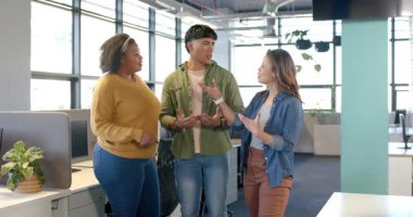 Çeşitli iş arkadaşları açık ofiste masa bölümlerinin yanında konuşma yapıyor, el kol hareketi yapıyor ve gülümsüyor. İşbirliği, takım çalışması, iletişim, modernlik, profesyonellik, gündelik, pozitiflik