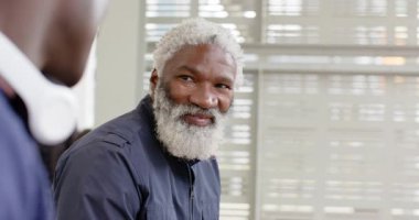 Afrika kökenli Amerikalı bir adam, ofisteki meslektaşlarına kulaklıklar ve perdelerle gülerek tepki veriyor. Profesyonel, işbirliği, iletişim, modernlik, olumlu, katılım, çalışma alanı