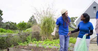 Çeşitli gönüllüler, halk bahçesindeki yeşil torbalara yabani otları yerleştiren bir adama tepki veriyor. Çevre, takım çalışması, sürdürülebilirlik, kırsal, açık hava, işbirliği, yeşillik
