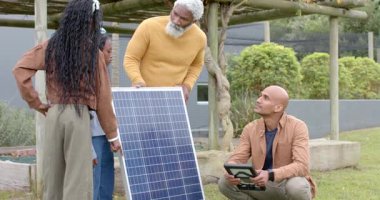 Aile ve kurucu bahçedeki güneş panelini sabitliyor ve tablet üzerindeki hücreleri kontrol ediyor. Açık hava, sürdürülebilirlik, yenilenebilirlik, teknoloji, çevre dostu, modern, doğal