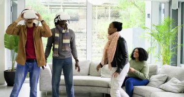 Evde VR kulaklık takan farklı arkadaşlar var. Bu arada kadın sanal deneyim için kemerleri sıkıyor. Teknoloji, yenilik, sosyal, eğlence, rahatlama, modernlik, dijital