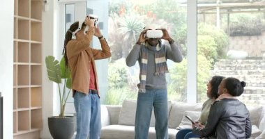 VR kulaklıklarıyla eve giren çeşitli arkadaşlar VR dünyasını keşfederken diğerleri tableti tıkırdatıyor. Teknoloji, yenilik, etkileşim, işbirliği, eğlence, modern yaşam tarzı