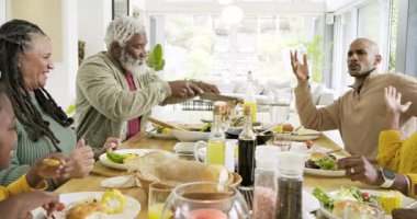 Çeşitli aile yemekleri yemek için yemek masasında toplanıyor, insanların salata kepçelemesine ve ekmek vermesine neden oluyor. Aile, toplanma, yemek, kutlama, bağlantı, birliktelik, iç mekan.