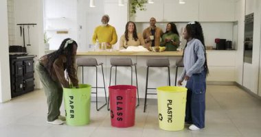 Çöp kutularını ayırırken, iki Afro-Amerikalı kız mutfak adasında ailelerine sarılarak beşlik çakıyor. Geri dönüşüm, sürdürülebilirlik, aile, toplum, takım çalışması, çevre, çevre dostu