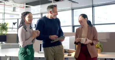 Muhtelif iş arkadaşları ofiste karşılıklı selamlaşırken fincanlar kırılma ve gülme tabletini işaret ediyor. İşbirliği, takım çalışması, iletişim, modern, üretkenlik, iş dünyası, içişleri