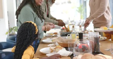 Yetişkin bir kadın kahvaltıda ekmeğini paylaşırken çeşitli aileler ahşap masada tabak dağıtıyor. Aile, yemek, yemek, birliktelik, konukseverlik, kırsal, yaşam tarzı