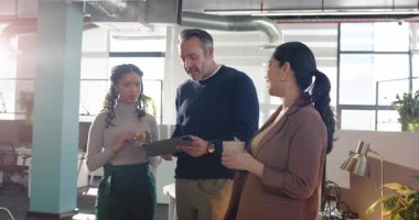 Muhtelif iş arkadaşları ofiste toplanıp kahve kupası tutarken tabletleri gözden geçiriyorlar. İşbirliği, takım çalışması, yenilik, modern, profesyonel, iletişim, beyin fırtınası.