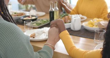 Çeşitli aileler ellerini sıkarak teşekkür ediyor sonra da kızarmış tavukla masada el çırpıp sohbet ediyorlar. Aile, birliktelik, minnettarlık, topluluk, sıcaklık, kutlama, bağ.