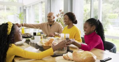 Masanın etrafında toplanmış çeşitli aileler el ele tutuşuyor, başlarını eğiyor ve ekmeği paylaşmadan önce teşekkür ediyorlar. Aile, birlik, kutlama, sıcaklık, birliktelik, yemek, kırsal