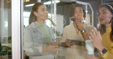 Çeşitli iş arkadaşları cam üzerinde diyagram akışı üzerinde çalışıyorlar. İşaretleyici, tablet ve kahve fincanı kullanıyorlar. İşbirliği, beyin fırtınası, yenilik, takım, modernlik, yaratıcı, üretkenlik