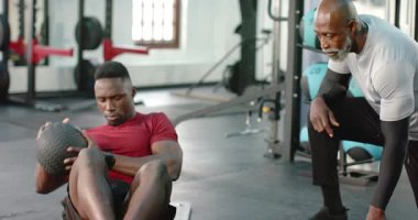 Afro-Amerikalı erkek müşteri paspasa vuruyor. Güç için antrenör üstüne ilaç topuna vuruyor. Fitness, strength, jimnastik, training, core, conditioning