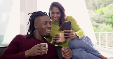 Çeşitli çiftler ellerinde kupa tutarken kadınlar balkonun yanındaki adama akıllı telefon içeriğini gösteriyor. Samimi, yaşam tarzı, minimalist, modern, samimiyet, mutluluk, bağlantı