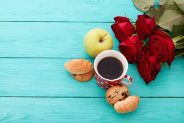 Cup of coffee with croissants and cookies and red roses on blue wooden background. Copy space. Mock up. Top view. Valentine mother day.