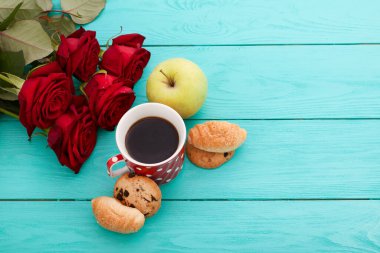 Cup of coffee with croissants and cookies and red roses on blue wooden background. Copy space. Mock up. Top view. Valentine mother day.