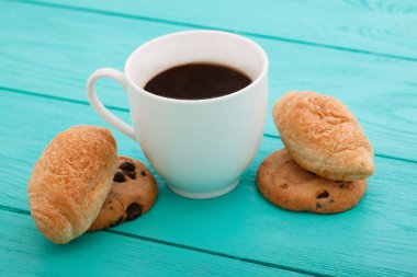 Cup of coffee with croissants and cookies and red roses on blue wooden background. Copy space. Mock up. Top view. Valentine mother day.