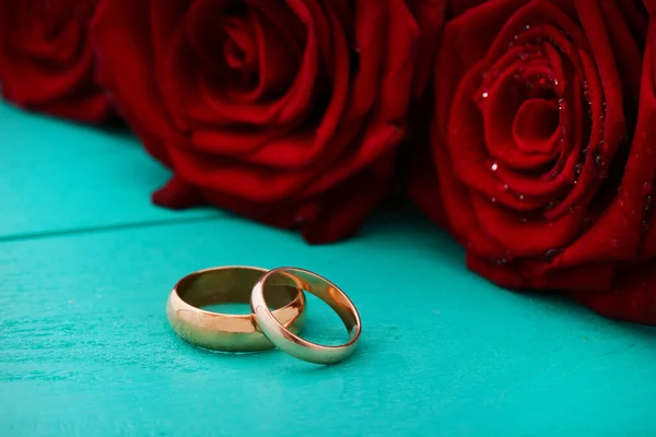 Wedding rings and red roses. Wedding bouquet on blue wooden background. Selective focus. Copy space
