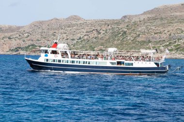 Turistli beyaz turist gemisi, dağların ve plajın arkasında denizde bir yerlere yelken açıyor.