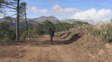 Koyu saçlı kadın elinde testereyle kırsalda yürüyor.