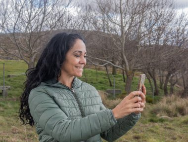 İspanyol esmer bir kadının gülümseyerek cep telefonuna bakması.