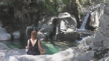 Doğada yoga yapan bir kadın, turkuaz bir dağ nehrinin önünde kayaların arasından yavaşça akıyor. Gredos Dağları