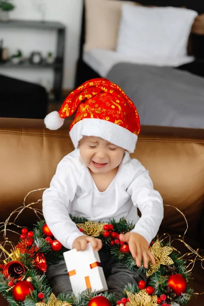 Christmas child opens a gift, happy boy tries to open a box of gifts. The boy tries to open the box of gifts, but it does not work. A well-packaged gift. A child cant open a Christmas present and