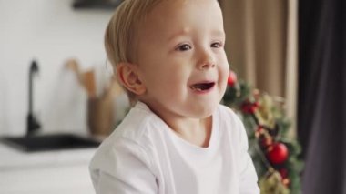 Küçük çocuk Noel kurabiyesi yer ve kendini şımartır. Kahkaha atar, ağzını açar ve ne yediğini gösterir..