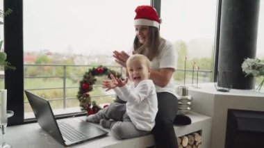 Çevrimiçi Noel. Anne ve oğlu dizüstü bilgisayarla internet üzerinden aileleriyle iletişim kuruyor. Noel 'de görüntülü konuşma. Küçük çocuk Noel 'de elini dizüstü bilgisayara sallıyor..