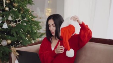 Genç bir kadın Noel arifesinde ailesiyle internetten gülüp etkileşime geçiyor. Bir kız kafasına Noel Baba şapkası takıyor..