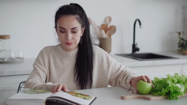 一个年轻的女人在节食 这个女人是个素食主义者 读一本关于健康饮食和生活方式的杂志 健康饮食 一个年轻的女人吃了很多蔬菜 自我照顾 看杂志的女人 — 图库视频影像