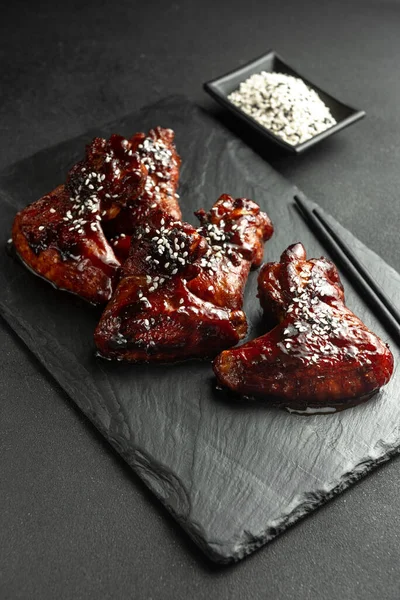 Asian-style chicken wings in sour sweet sauce on a plate on a dark stone background with space to copy. Top view, flat plan. Sticky honey-soy chicken wings on plate over dark stone background. Top